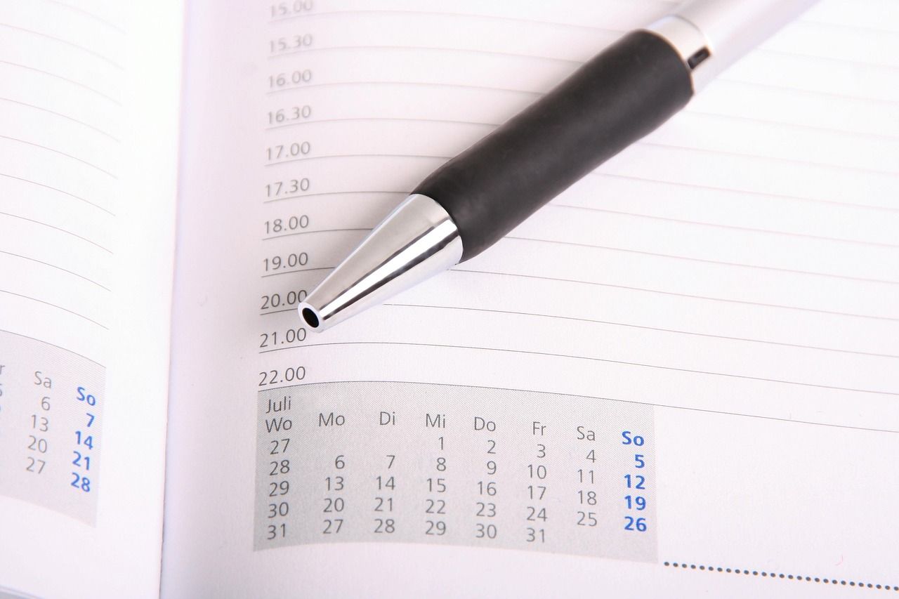 A hand writing a schedule into a planner next to a calendar