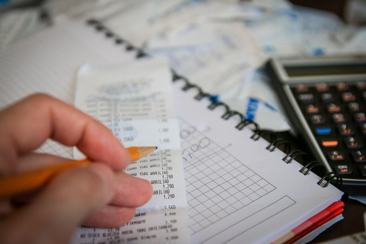 A hand working through utility bills and receipts next to a calculator